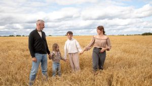 Happy family walking hand in hand through a golden wheat field on a sunny day.